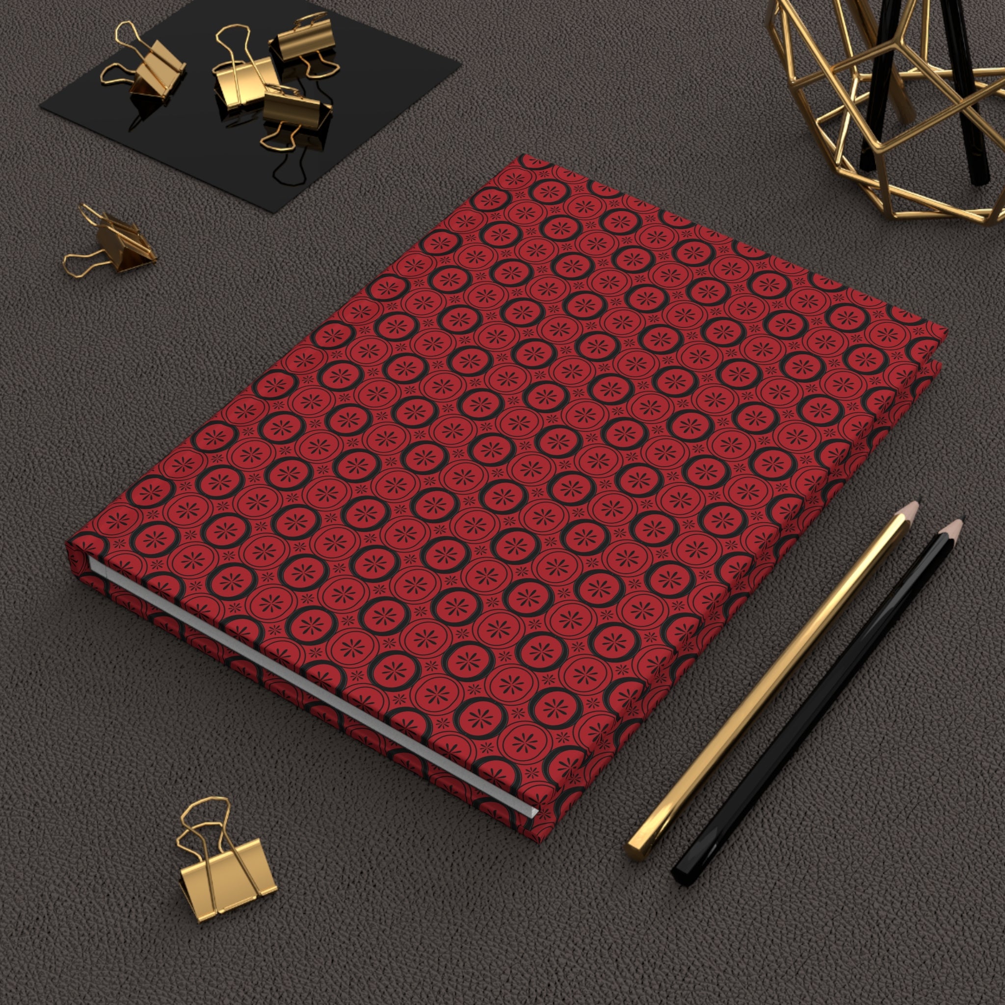 Red patterned notebook with gold and black office supplies on a dark surface