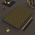 Notebook with gold geometric pattern on a dark surface with office supplies.