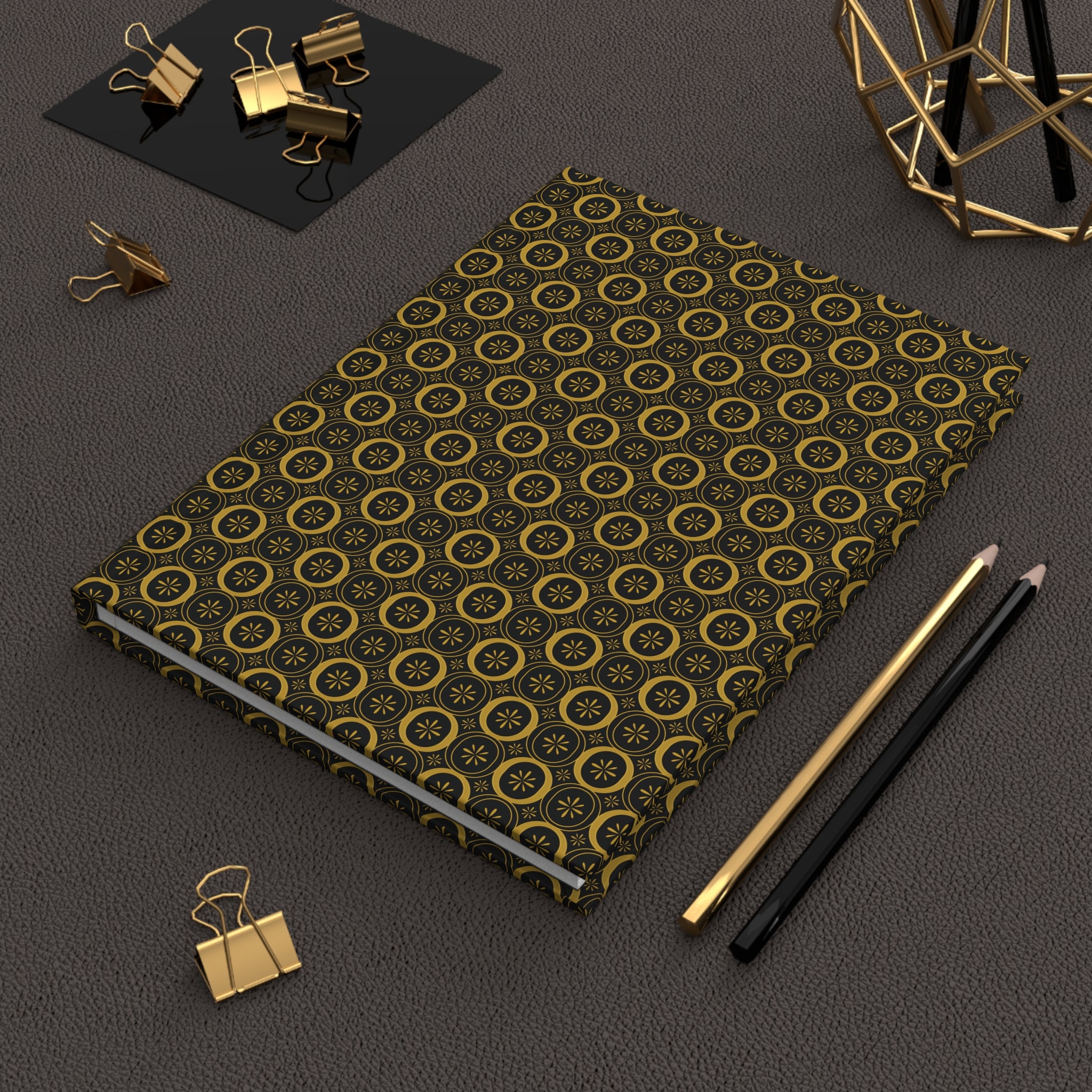 Notebook with gold geometric pattern on a dark surface with office supplies.
